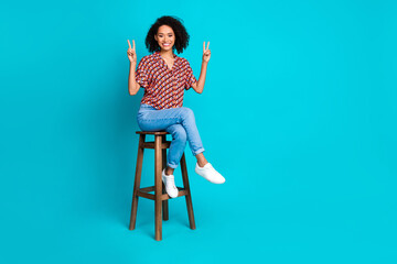 Photo of positive girl sit chair make v sign isolated cyan color background