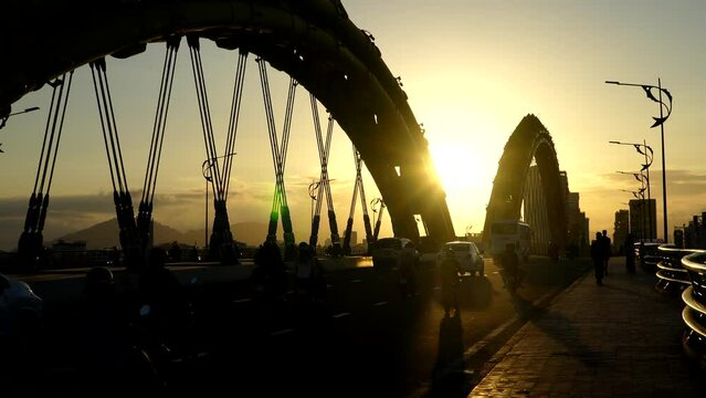 Da Nang, Vietnam - March 9, 2024: Traffic of mopeds and cars driving on the Dragon Bridge during sunset