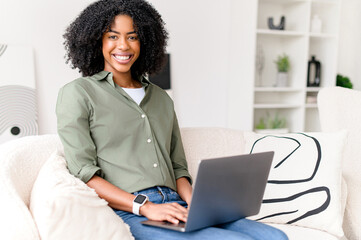 In a moment of joyful online interaction, an African-American woman smiles while working on her...
