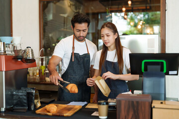 Coffee shop,with male and female workers in denim aprons, sharing a task; one placing pastries...
