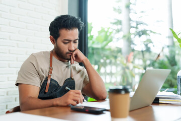 Multiethnic male business employee, brown shirt, overalls, cafe owner Sitting working  tablet...