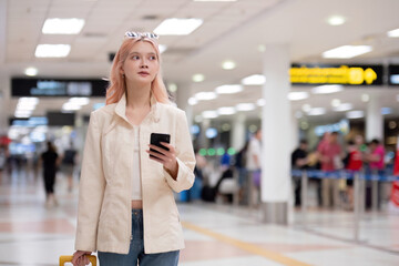 Young traveler with smartphone and luggage at airport terminal. Concept of modern travel,...