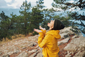 A joyful woman in a vibrant yellow jacket celebrating on top of a majestic mountain peak