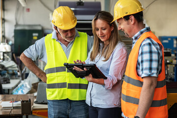 A supervisor stands confidently with workers on the factory line, using a tablet to check the...