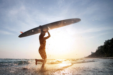 Female surfer wearing a swimsuit holding a surfboard on her head, entering out of sea after surfing...