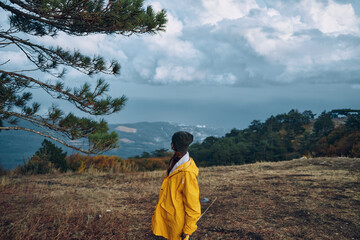 A man in a yellow raincoat standing on a hill admiring nature's beauty with forest and mountains in background