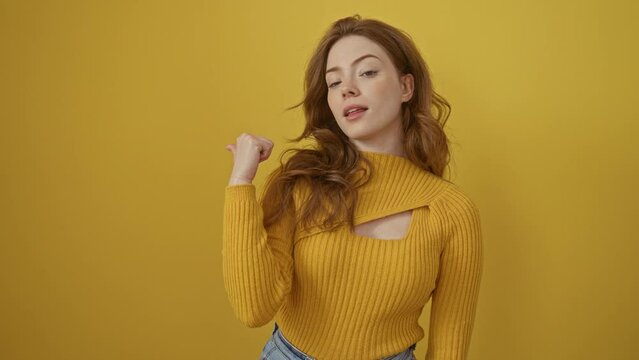 Young caucasian woman wearing sweater standing smiling with happy face looking and pointing to the side with thumb up. over isolated yellow background