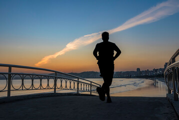 Sportsman Runner passing by the beach bridge over the water channel during sunset. In the background the sand strip and the waterfront buildings in the City of Santos, Brazil.