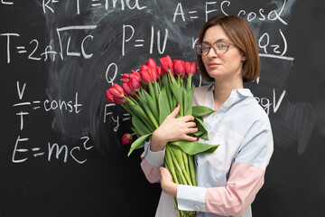 A young attractive teacher stands with a bouquet of flowers in the classroom. Teachers day and...