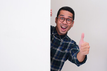 A man peeking behind white billboard with excited expression and give thumbs up