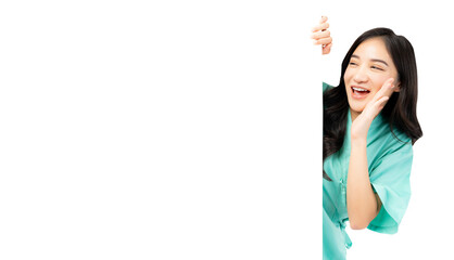 Cheerful young Asian female nurse peeking around a blank whiteboard, smiling and calling out, wearing green medical scrubs. The image captures a friendly healthcare professional in a playful 