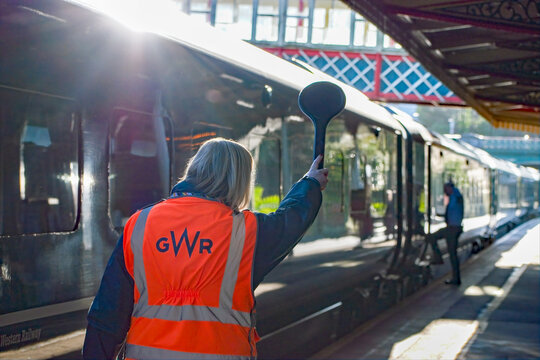 Torquay, Devon, uk. January 2nd 2023 Railway train conductor waves a signal to a station platform guard allowing the train to safely leave the station. 