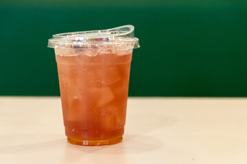 Iced tea in a plastic cup with a clear lid. The cup is sitting on a table. The background is green.