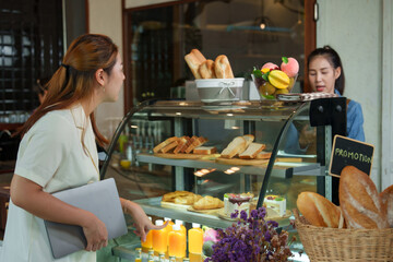 Beautiful female customer, Asian businessman She is buying bread, cakes, bakery, coffee shop, small business. She smiled happily. A beautiful Asian shop owner is taking orders behind a bread stand.