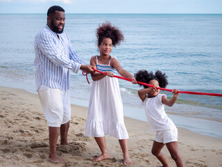 Happy African American family playing tug of war at the beach. People lifestyle travel on vacation...