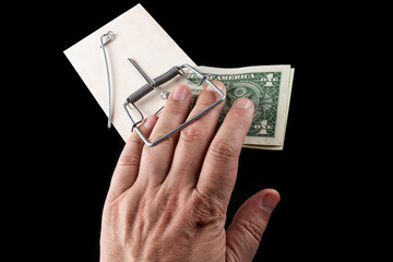 Man's fingers caught in a mousetrap and a 1 US dollar bill on a black background