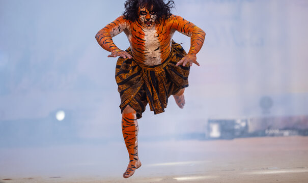 Portrait of an male artist performing classical dance kuchipudi as tiger to save himself from hunter on stage with tiger makeup on his  face and body.