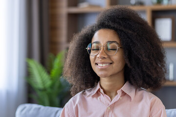 Young woman meditating at home, feeling calm, relaxed, and happy. Practicing mindfulness and...