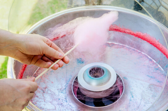 Close up view of person hands spinning pink color cotton candy with machine. Spin around wood stick outdoors in summer.

