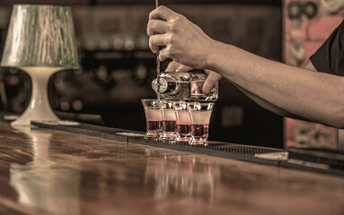 Shots at the nightclub. Barman preparing cocktail shooter. Bartender pouring strong alcoholic drink into small glasses on bar