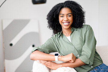 Seated casually on a couch, an African-American woman wears a delightful smile, arms folded...