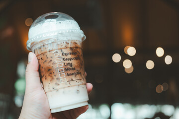 Cropped shot view of someone hand holding a plastic cup of iced coffee and showing a list of coffee...