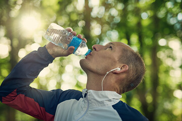 Running, fitness or man drinking water in park with earphones for music, wellness or training...