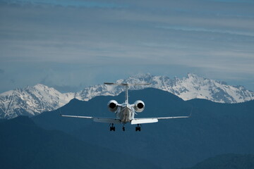 Airplane in flight against the backdrop of snow-capped mountains. The plane is preparing to land