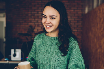 Cheerful female designer dressed in casual outfit holding mug of coffee while talking and...