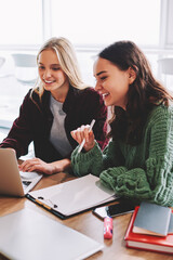 Positive female designers watching productive webinar together during working process sitting at laptop connected to wireless 4G internet.Successful young women collaborating on own project in office