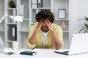 Man experiencing stress and frustration in office setting. Sitting at desk with laptop, feeling overwhelmed by workload.