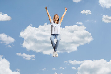 Happy young woman sitting on a cloud and raising arms