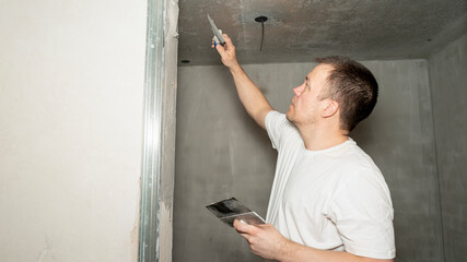 Worker is putting a gypsum plaster on a wall using a spatula. 