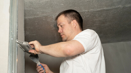 Worker is putting a gypsum plaster on a wall using a spatula. 