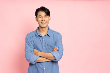 Smiling young Asian man in jeans shirt with arms crossed isolated on pink background