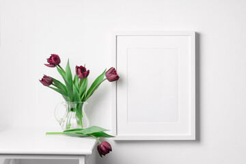 Vertical blank picture frame mockup on white wall with spring tulips flowers, copy space