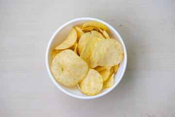 A bowl of salted crispy potato chips on a wooden background. Top view.