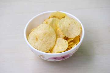 A bowl of salted crispy potato chips on a wooden background.