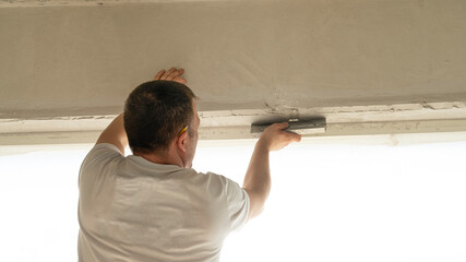 Worker is putting a gypsum plaster on a wall using a spatula. 