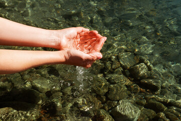 A woman touches the water with her hands. Women's hands collect water in their hands near the...