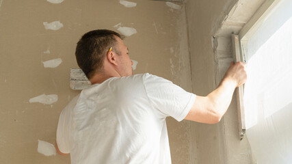 Worker is putting a gypsum plaster on a wall using a spatula. 