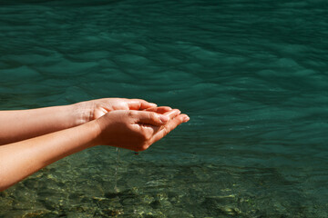 A woman touches the water with her hands. Women's hands, water is pouring near a river, sea, ocean....