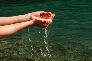 A woman touches the water with her hands. Women's hands, water is pouring near a river, sea, ocean....