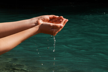 A woman touches the water with her hands. Women's hands, water is pouring near a river, sea, ocean....