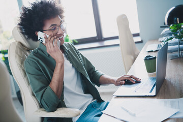 Photo of cheerful handsome agent dressed khaki shirt eyewear speaking modern gadget indoors...