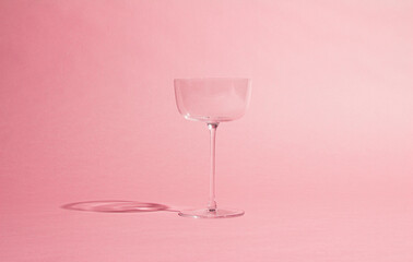 minimalist image of an empty glass goblet against a soft pink background. The simple and elegant...