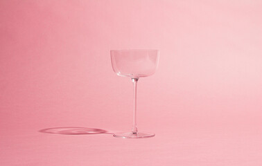 minimalist image of an empty glass goblet against a soft pink background. The simple and elegant composition is perfect for drink themes, style and modern design.