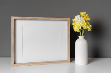 Blank wooden landscape frame mockup with daffodils flowers over grey wall interior, copy space for picture design