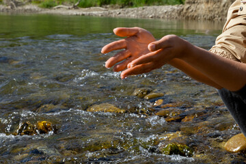 Women's hands, water is pouring near the river. People in nature. Ecology. A woman touches the water with her hands.