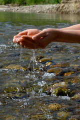 Women's hands, water is pouring near the river. People in nature. Ecology. A woman touches the water with her hands.